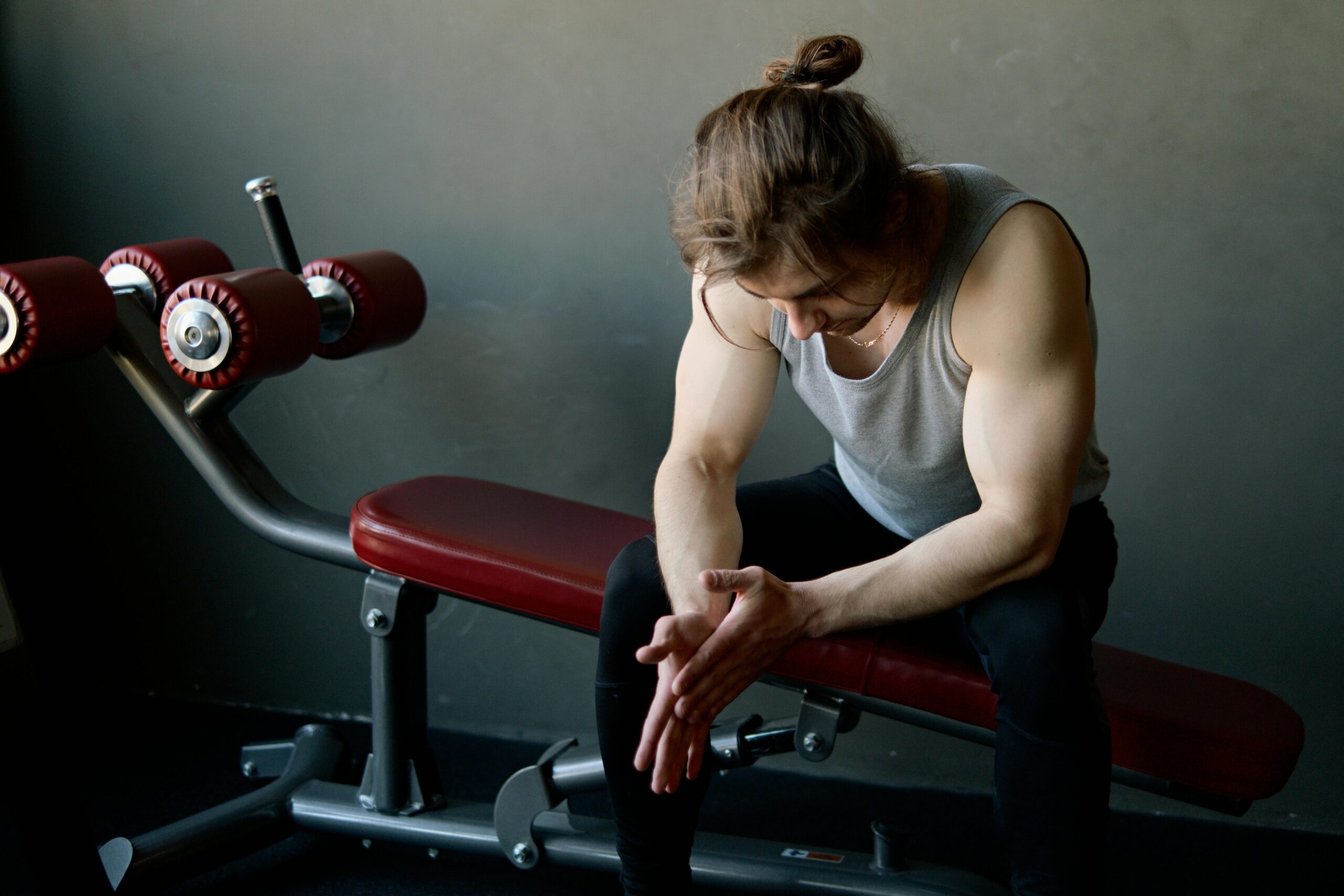 Tired athlete sitting on a gym bench after workout, representing the importance of sleep and recovery for fitness performance and muscle recovery.